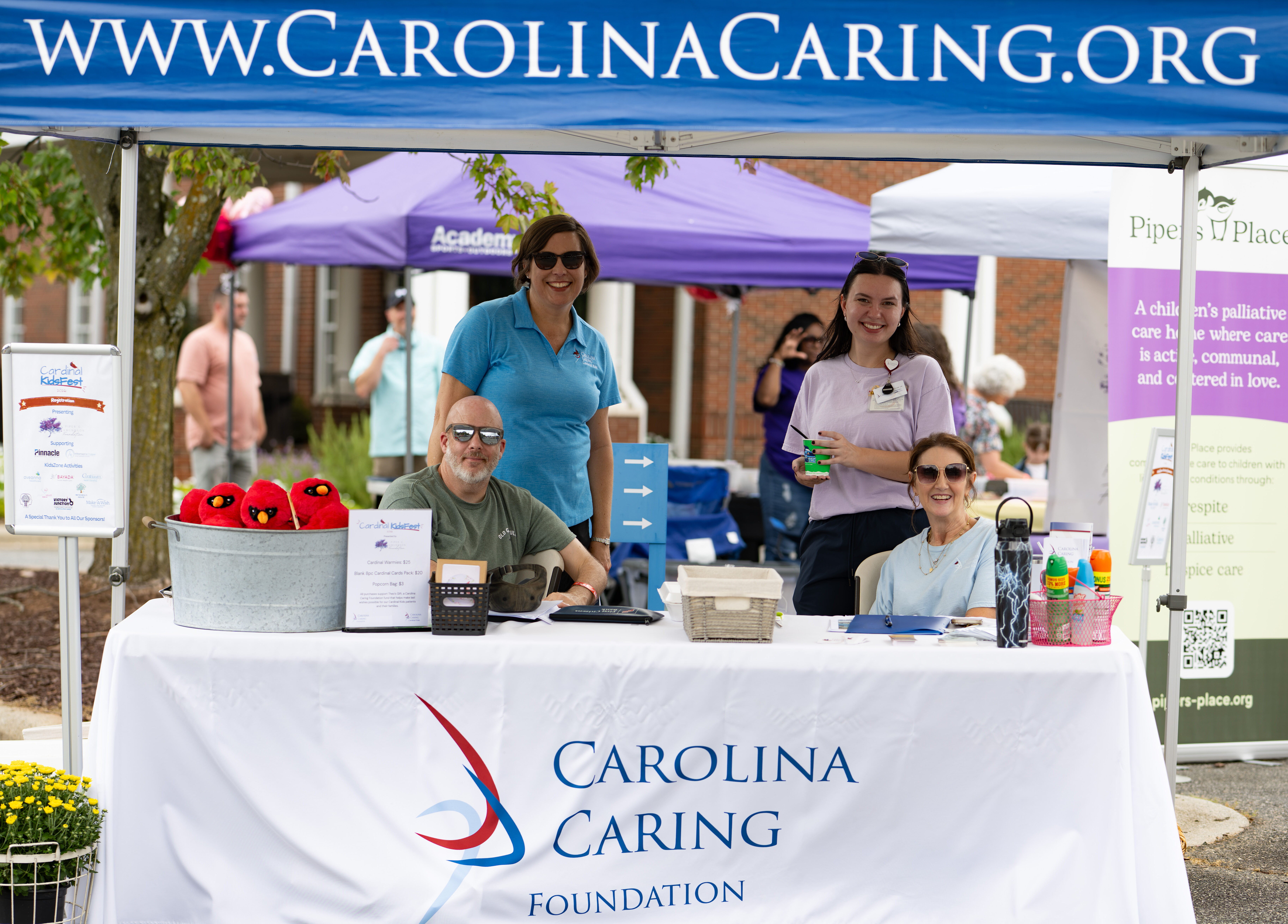 4 Carolina Caring Foundation team members gather at tent booth as they host the 2nd annual Cardinal KidsFest in Mooresville, NC.